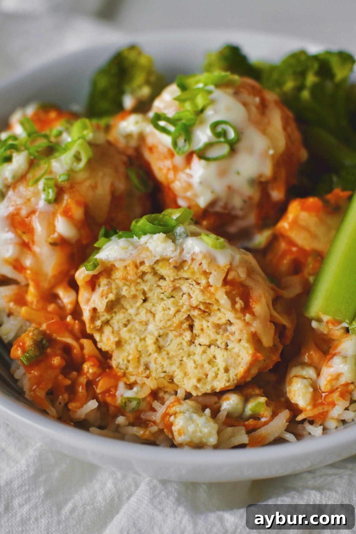 Spicy Buffalo Chicken Meatballs 2 Looking down at Buffalo Chicken Meatballs served in a bowl over ranch rice with a side of roasted broccoli and celery, one of the meatballs has a bite taken from it.