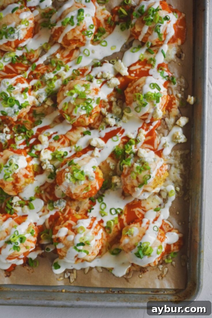 Looking down at a full tray of Buffalo Chicken Meatballs just out of the oven after melting the cheese and topped with chopped green onions and ranch dressing.