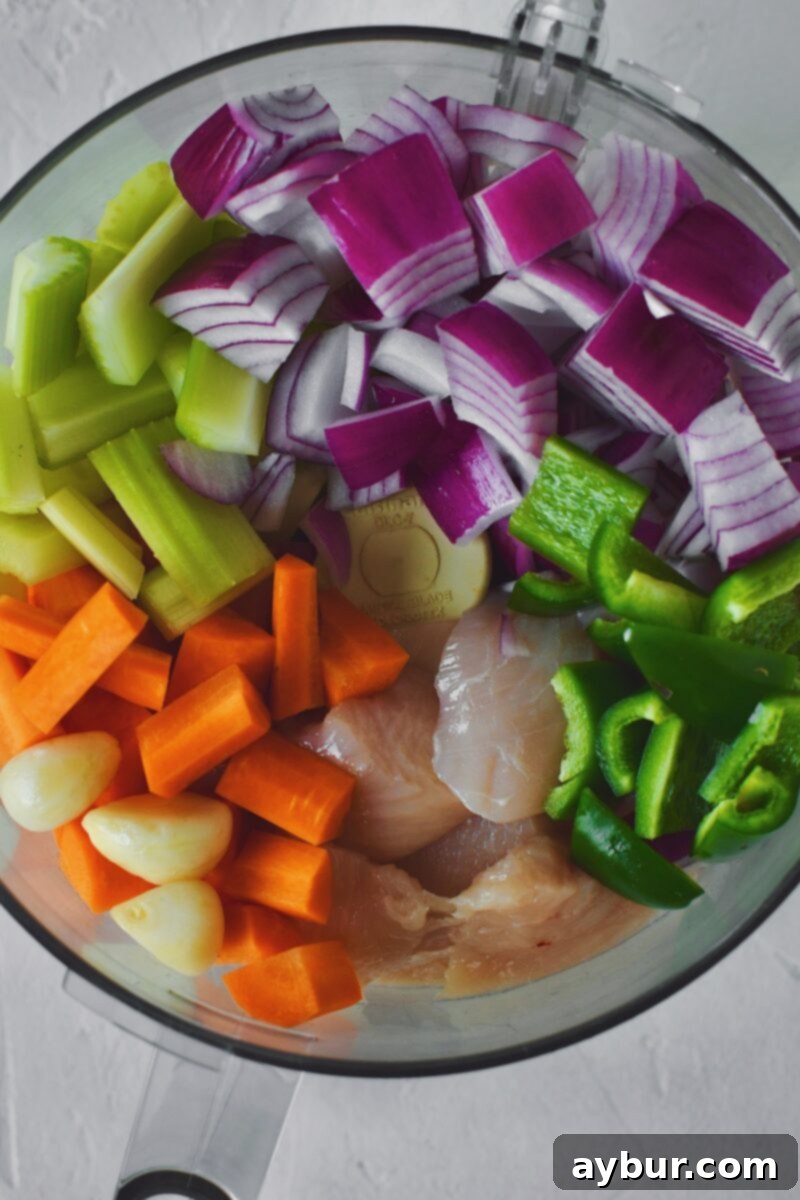 Diced Chicken, added to a food processor bowl, with the jalapeno, red onion, celery, carrot, and garlic, before pulsing together.