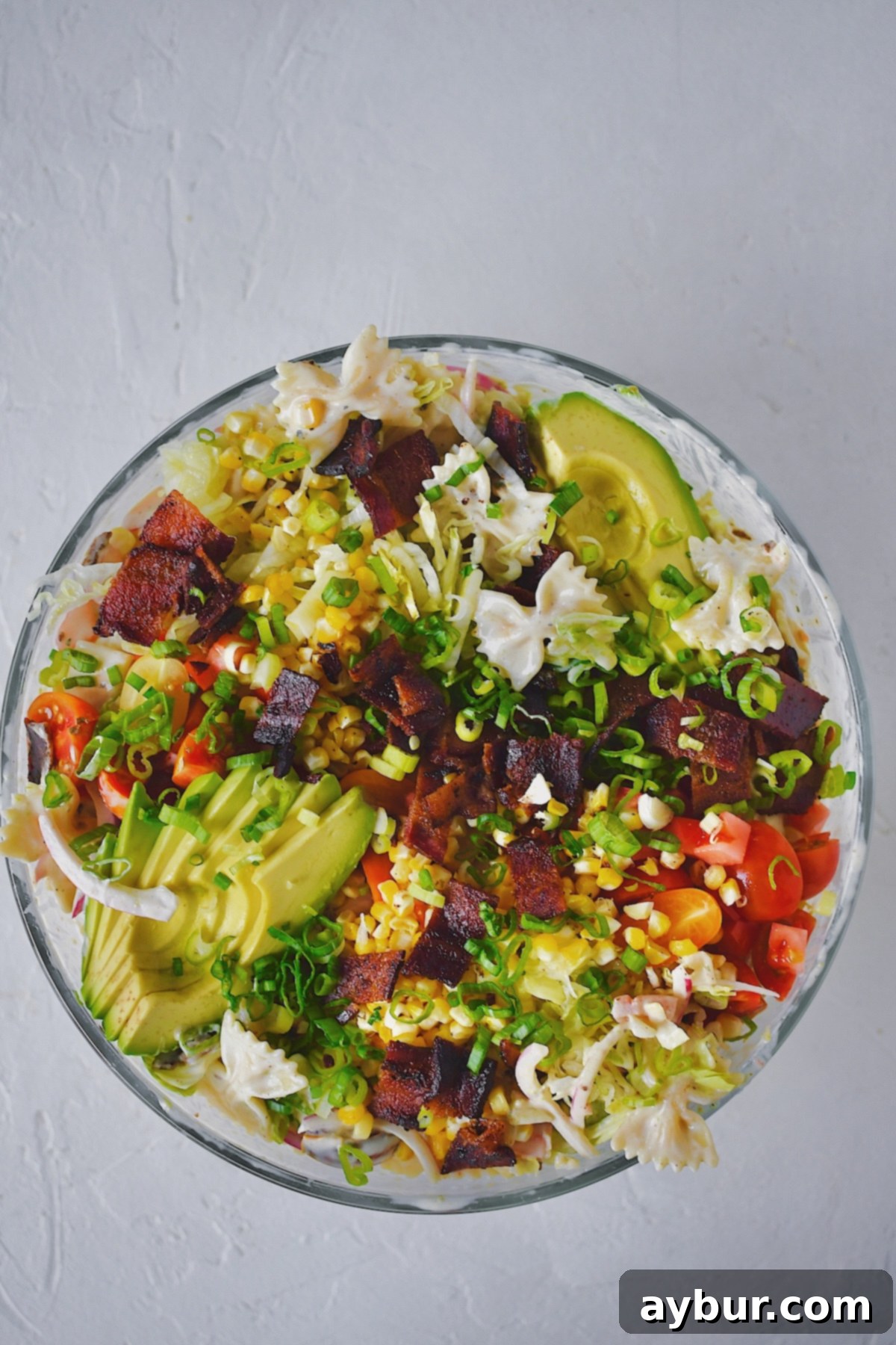 A vibrant bowl of BLT Pasta Salad, generously topped with crispy bacon, diced tomatoes, fresh green onions, and creamy avocado slices, ready to be served.