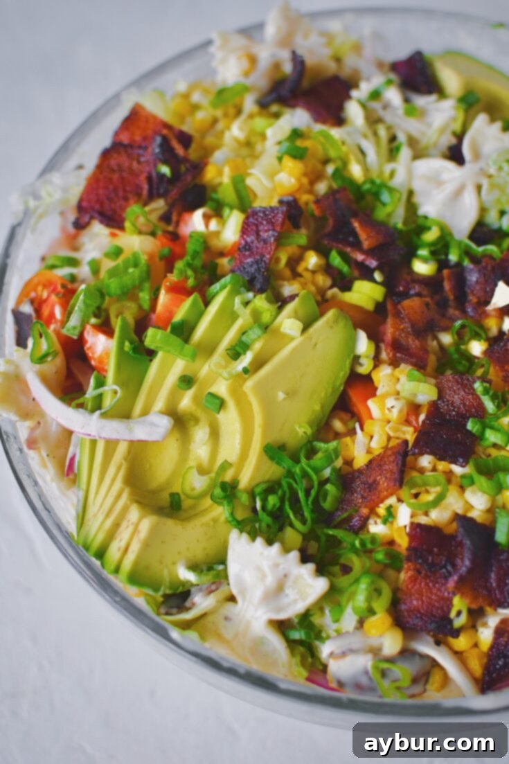BLT Pasta Salad, topped with more of the filling ingredients, avocado fanned on top, in a large bowl, ready to serve.