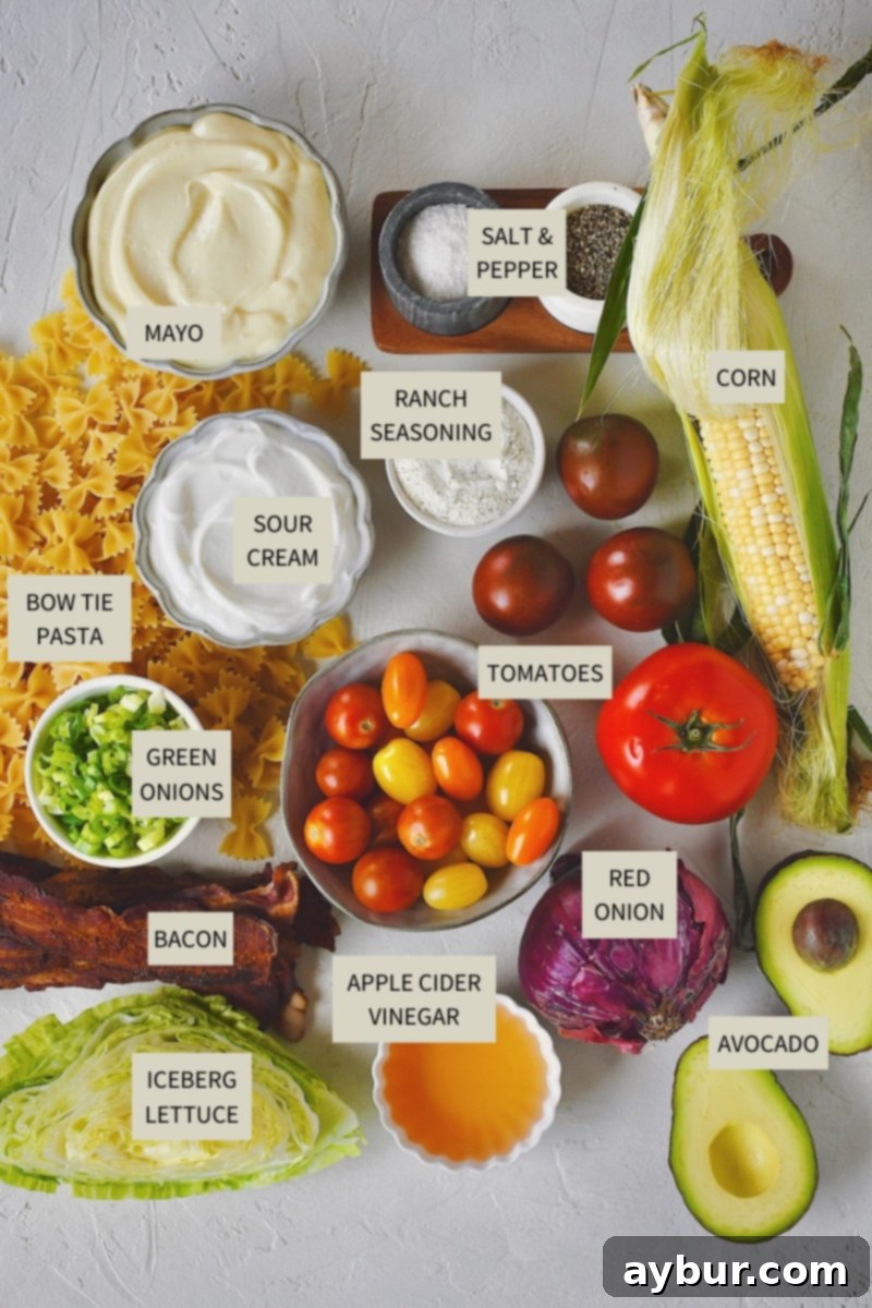 A selection of fresh ingredients neatly arranged on a counter, including ears of corn, ripe avocados, various tomatoes, crispy bacon, pasta, onions, and dressing components, all ready for making BLT Pasta Salad.