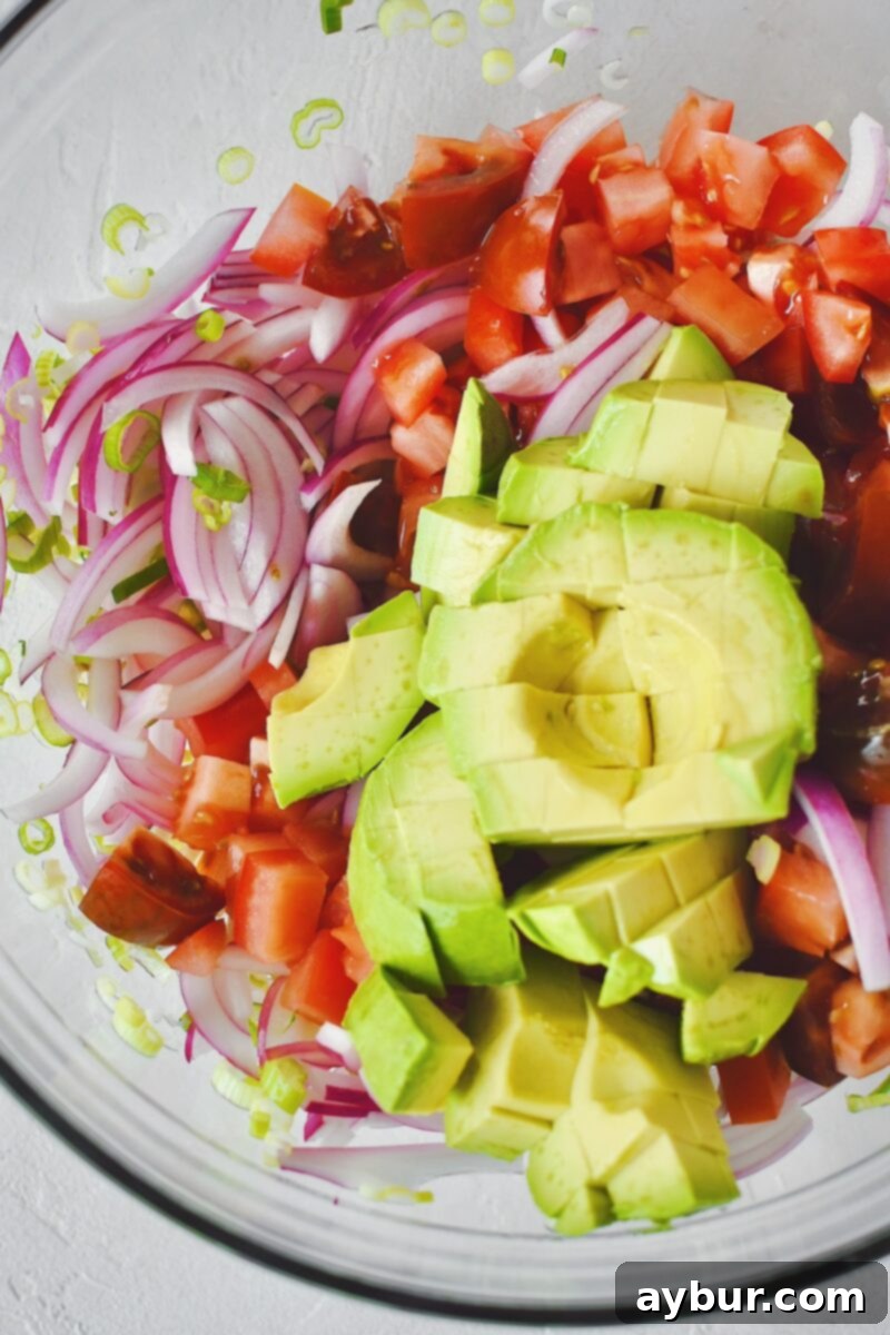 First, mixing the red and green onions, diced tomatoes, and diced avocado with apple cider vinegar in a large mixing bowl.