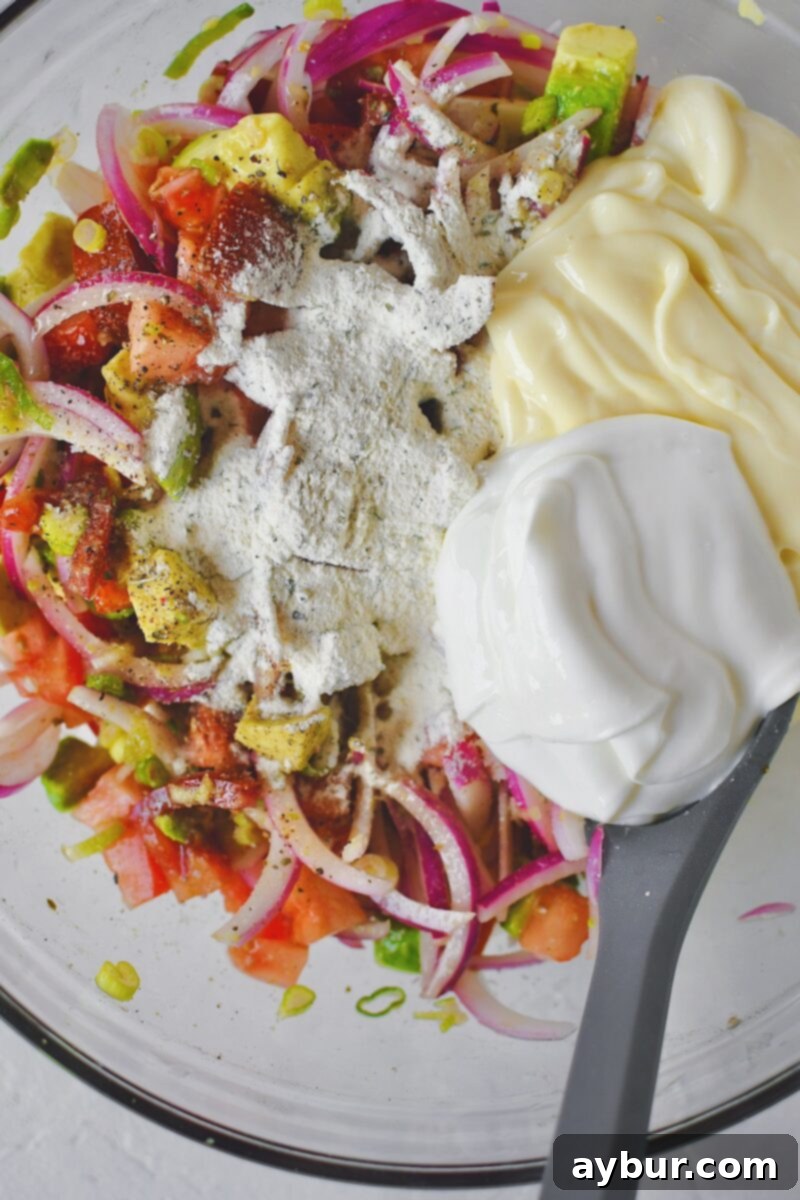 Making the creamy ranch dressing directly in the bowl by adding ranch seasoning, sour cream, and mayonnaise to the vinegar-coated vegetables.