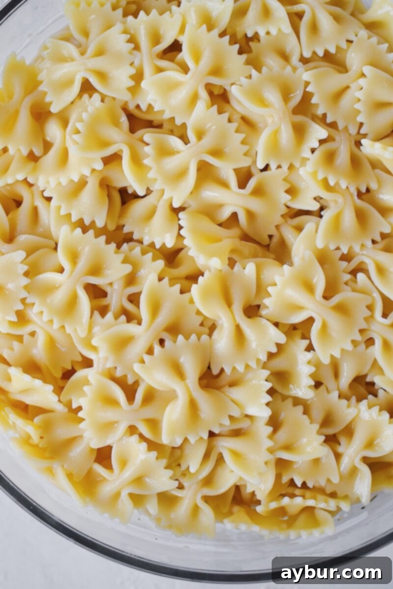 Adding perfectly cooked and cooled pasta to the large mixing bowl containing the dressed vegetables and ranch base.