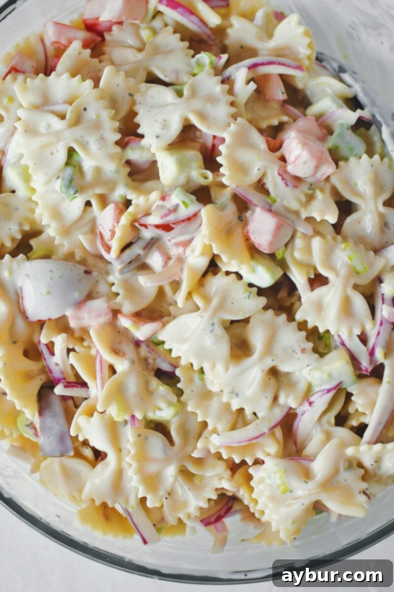 Tossing the base pasta salad thoroughly, ensuring the pasta is evenly coated with the creamy dressing, onions, tomatoes, and avocado.