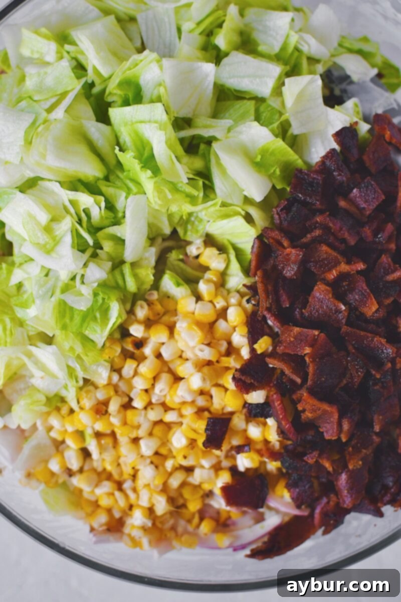 Lastly, gently mixing in the crispy bacon, fresh iceberg lettuce, and grilled corn into the prepared pasta salad before serving.