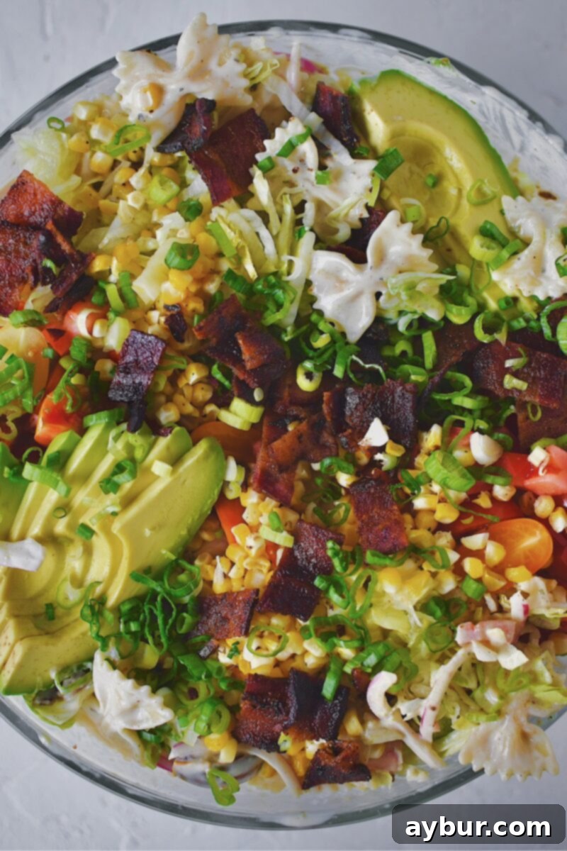 A beautifully presented large bowl of BLT Pasta Salad, garnished with extra avocado, bacon, corn, tomatoes, and green onions, perfectly ready to eat!