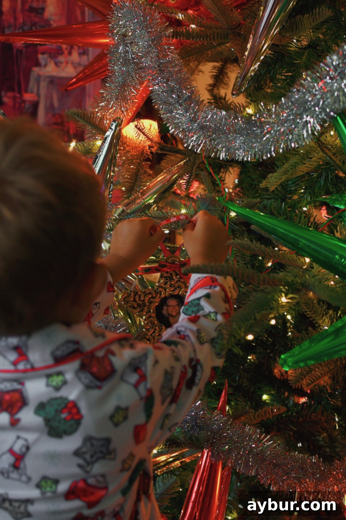 A child admires a pasta Christmas ornament on a decorated tree.