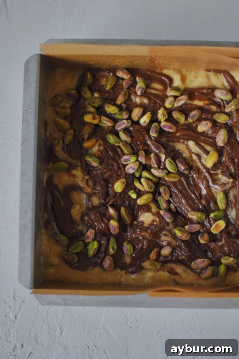 Batter placed in the prepared baking pan, topped with nutella that has been swirled in and topped with pistachios.