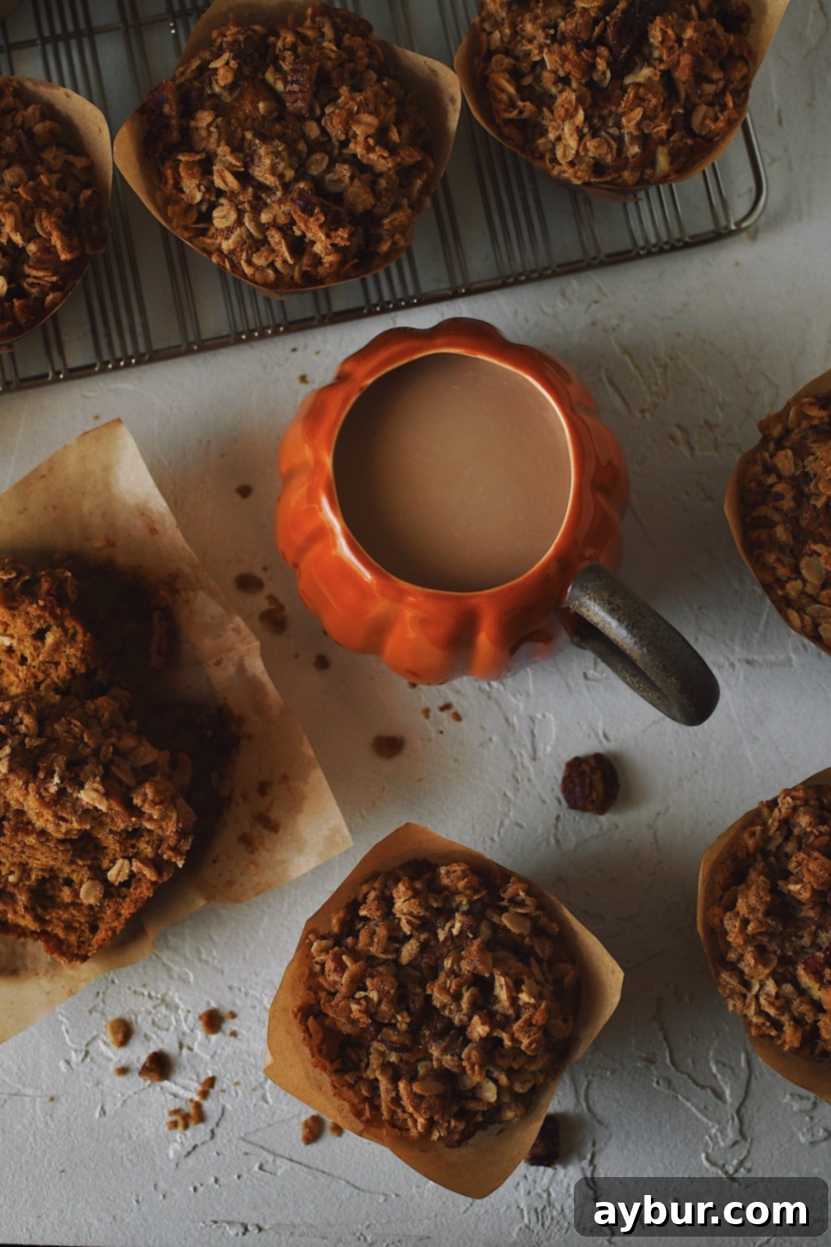 Pumpkin Banana Muffins with Pecan Streusel Topping 3 A close-up view of a collection of Pumpkin Banana Muffins, one expertly split to show its soft interior, alongside a pumpkin-themed coffee cup, perfect for a cozy autumn morning.