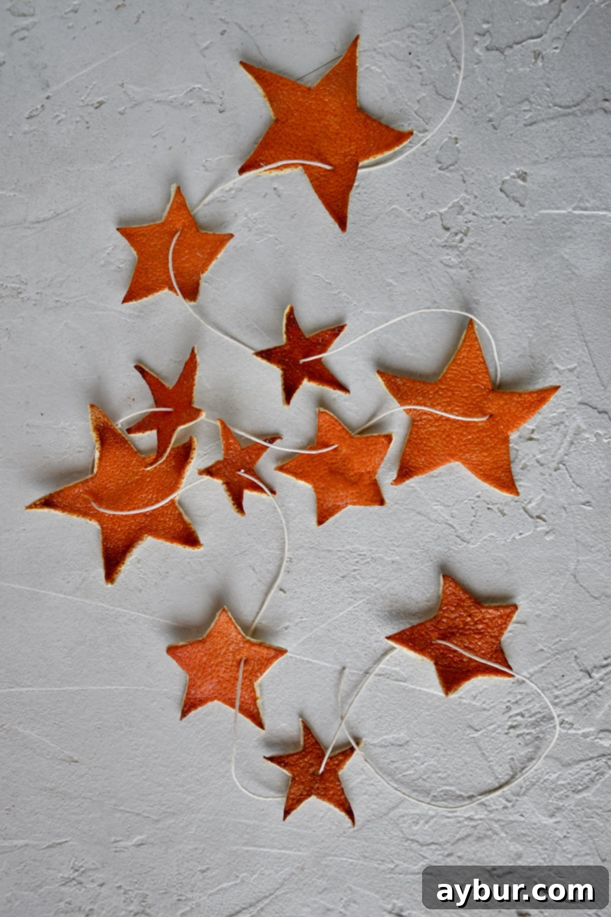 Fragrant Orange Star Garland 13 A beautifully assembled Orange Peel Star Garland, featuring varied star sizes strung on twine, gracefully laid out and ready to be draped on a Christmas tree or other festive display.