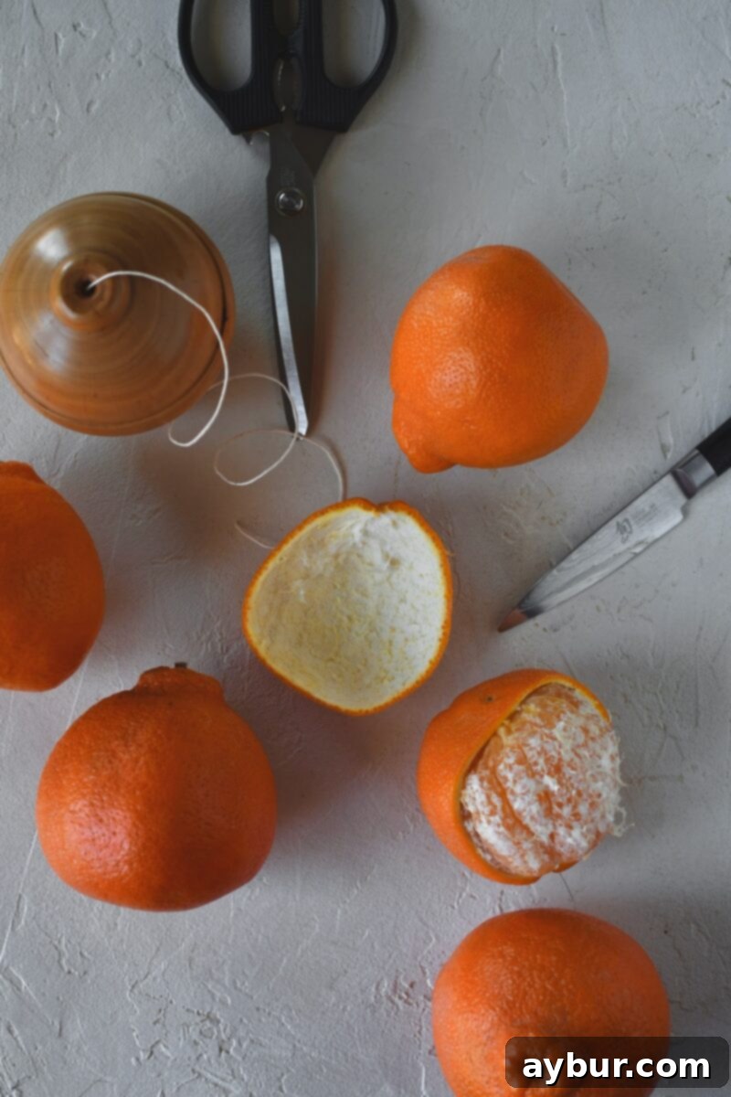 Fragrant Orange Star Garland 4 Fresh oranges arranged on a table, with one orange skillfully peeled, demonstrating the desired large, intact peel pieces for crafting the garland.