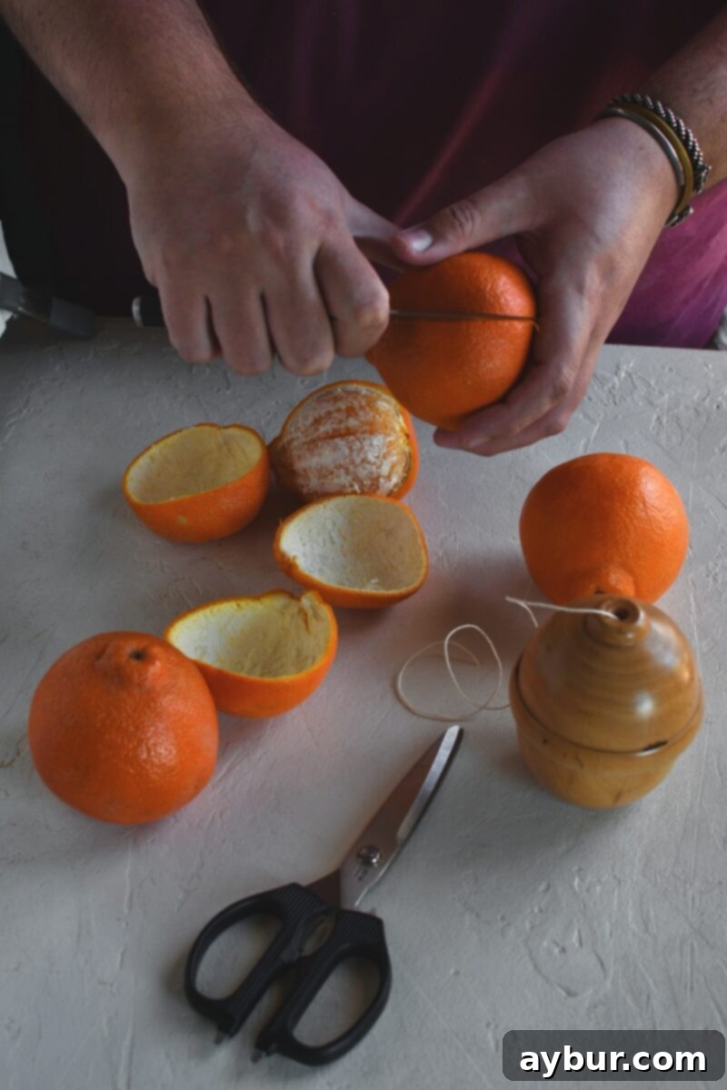 Fragrant Orange Star Garland 5 Close-up view of a hand gently slicing into an orange peel, ensuring only the skin is cut, a vital step for clean peel removal.
