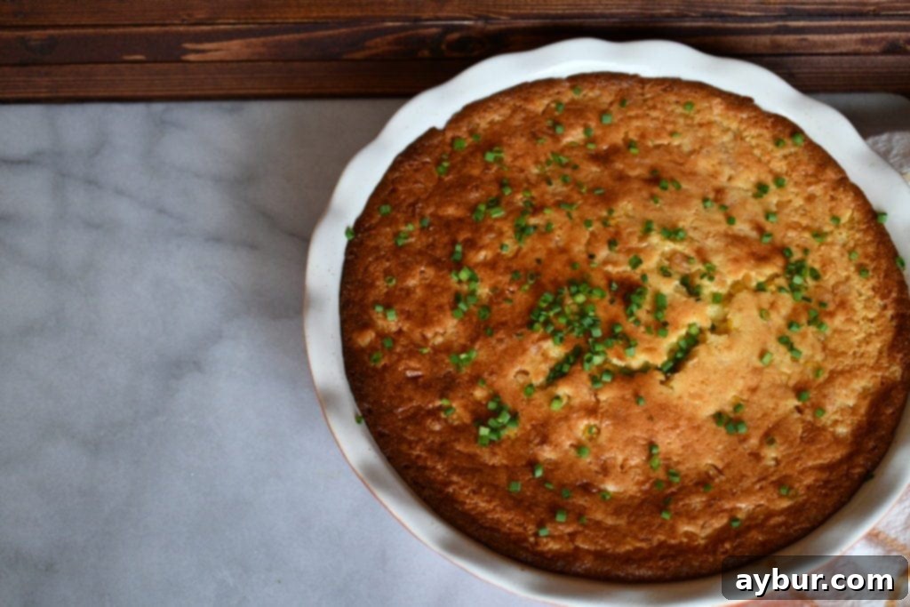 A golden brown, baked spoonbread in a white ceramic dish, ready to be served.