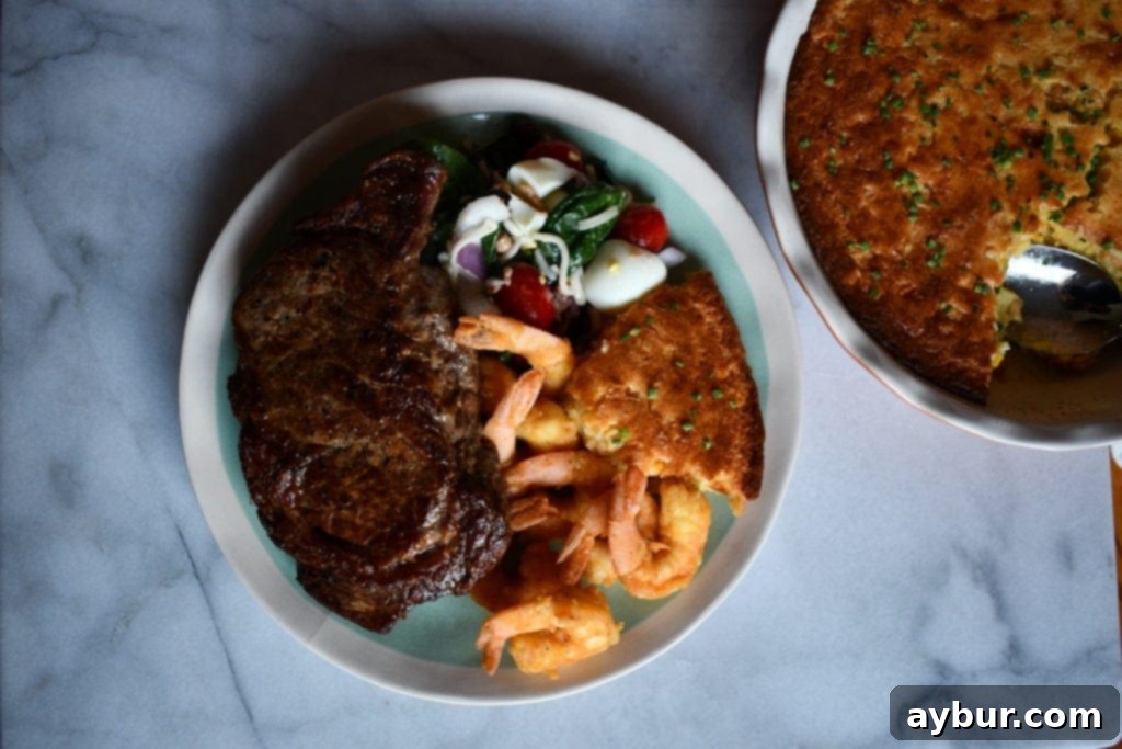 A Father's Day dinner table spread with Ribeye steaks, shrimp, salad, and the spoonbread in a serving dish.
