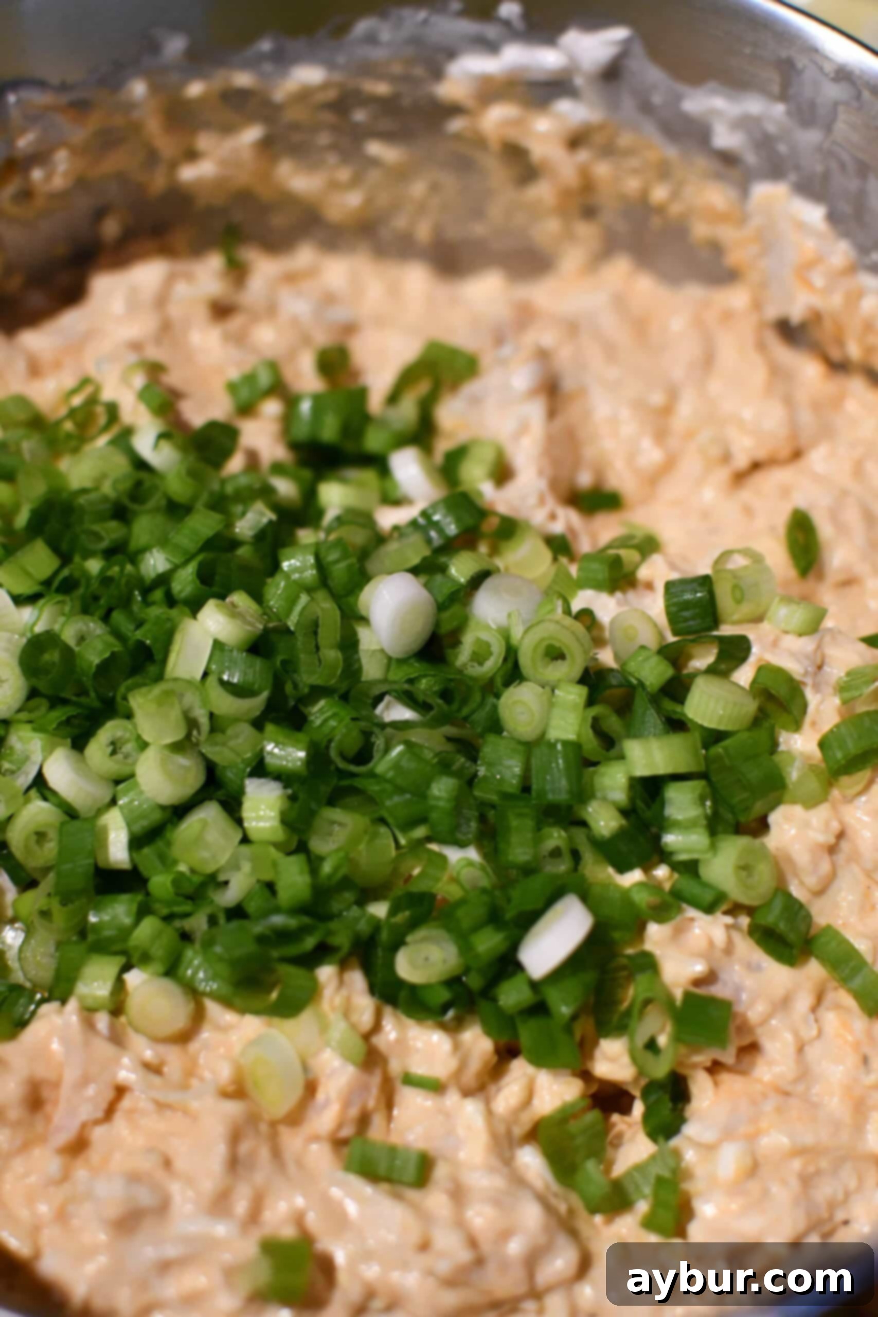 Adding fresh green onions to the creamy buffalo chicken cheese dip mixture.