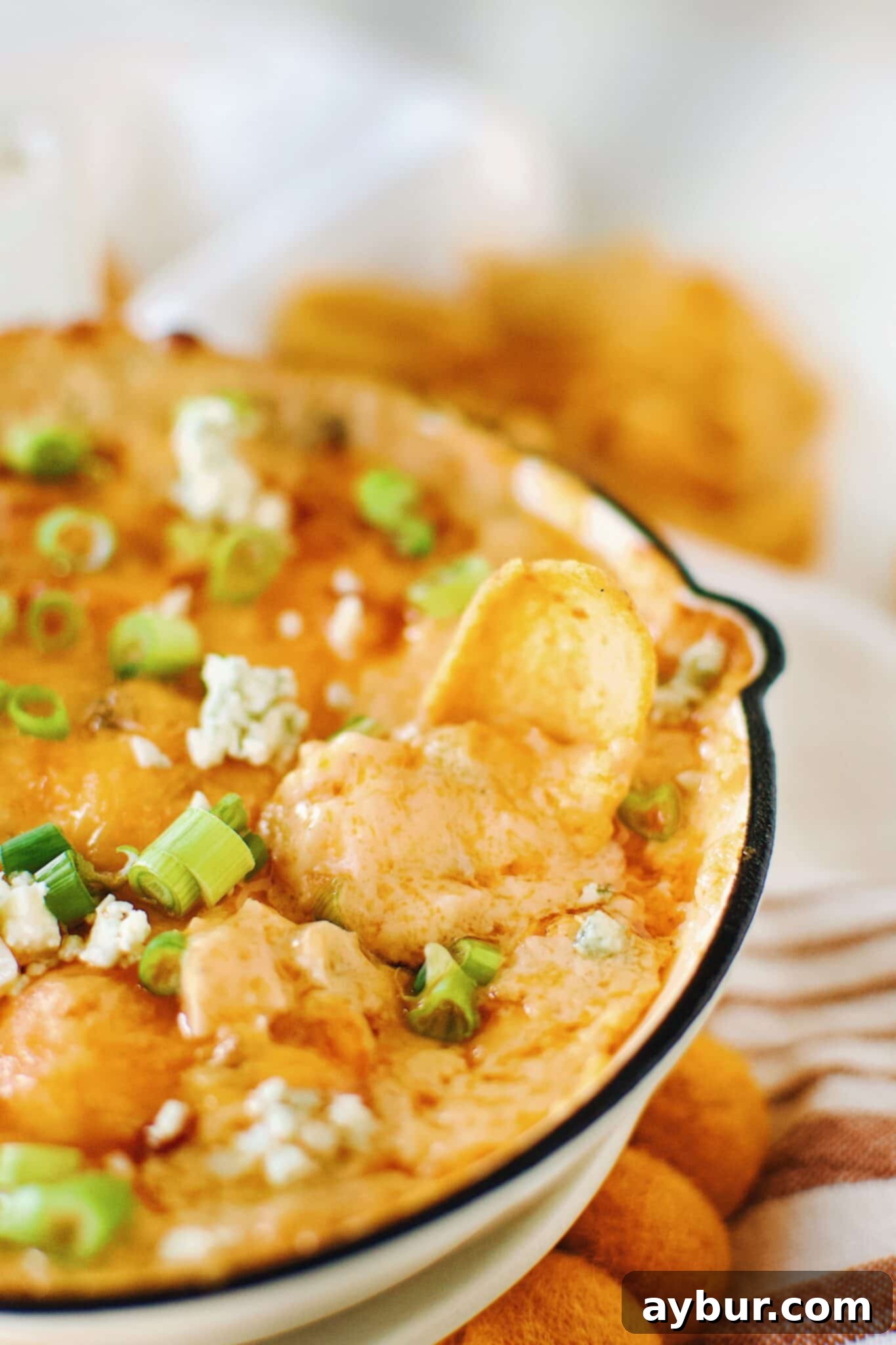Digging into warm, bubbly Buffalo Chicken Cheese Dip with a scoop chip for a perfect bite.