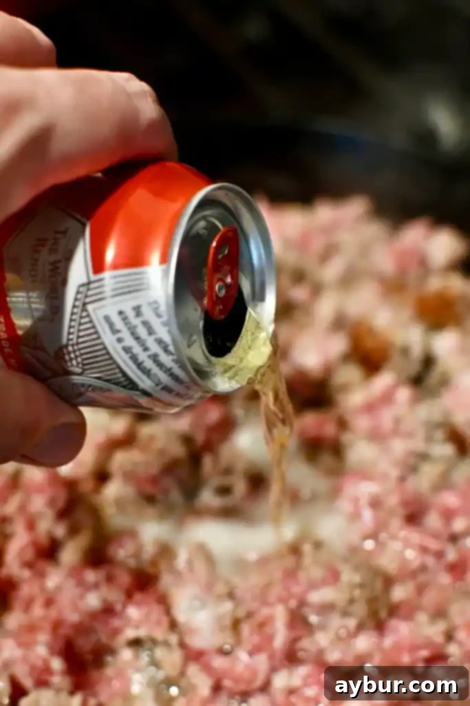 Close-up of bratwurst being deglazed with beer in a hot pan, creating a rich base for the lasagna sauce