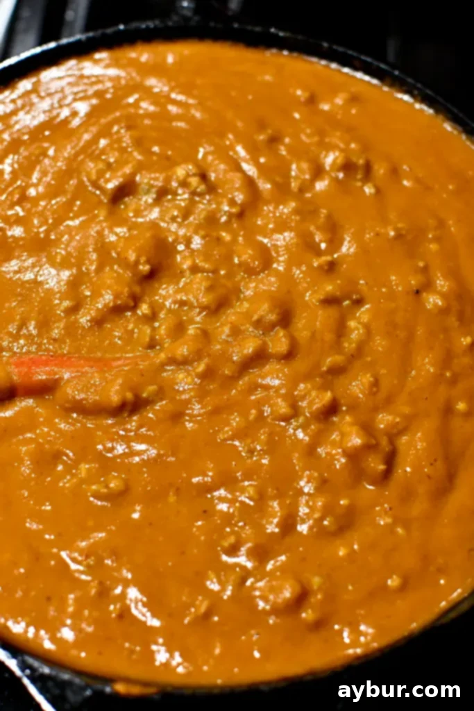 Pumpkin Beer Cheese and Bratwurst sauce simmering in a pan, rich orange hue with flecks of browned sausage
