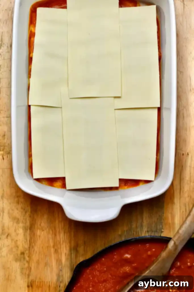 Detailed shot of layering the lasagna with noodles, sauce, and cheese mixture in a baking dish
