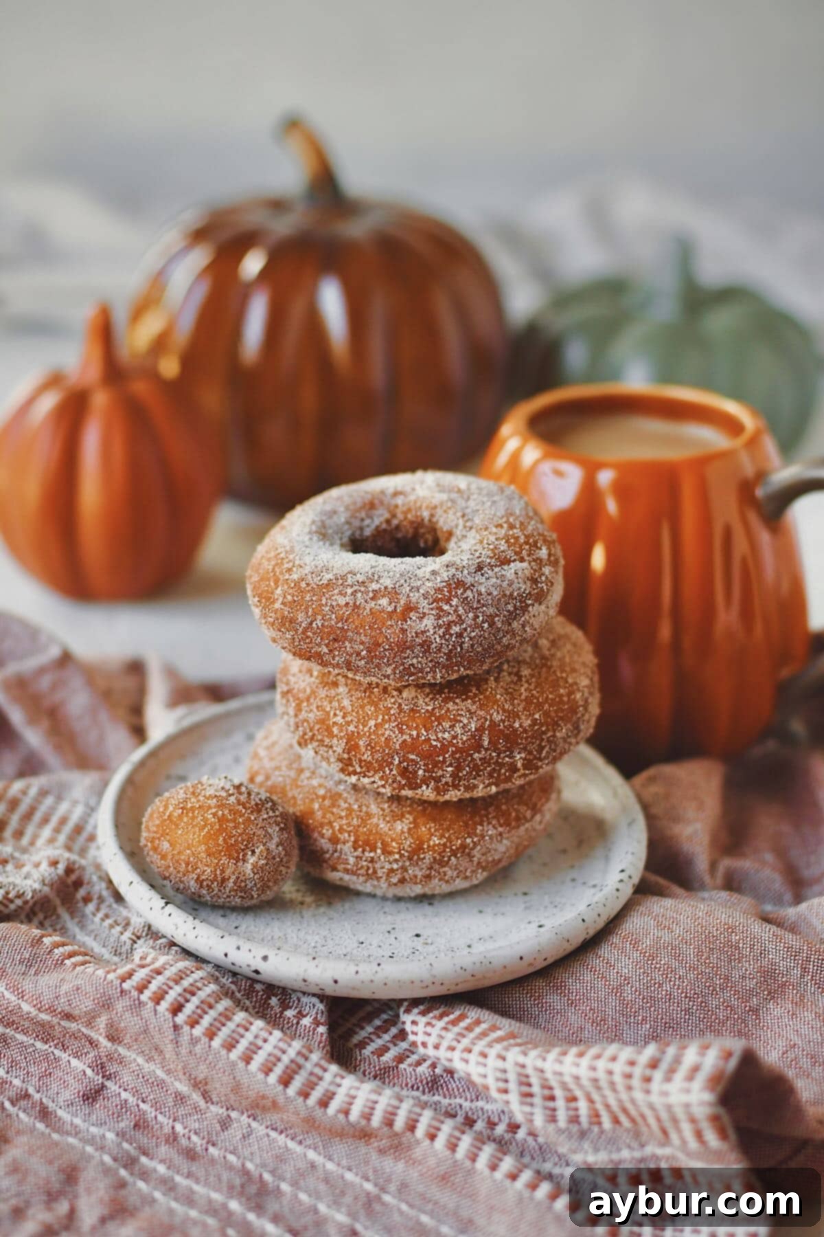 Pumpkin Donuts stacked up with a donut hole on the side, in front of a cup of coffee in a pumpkin mug.
