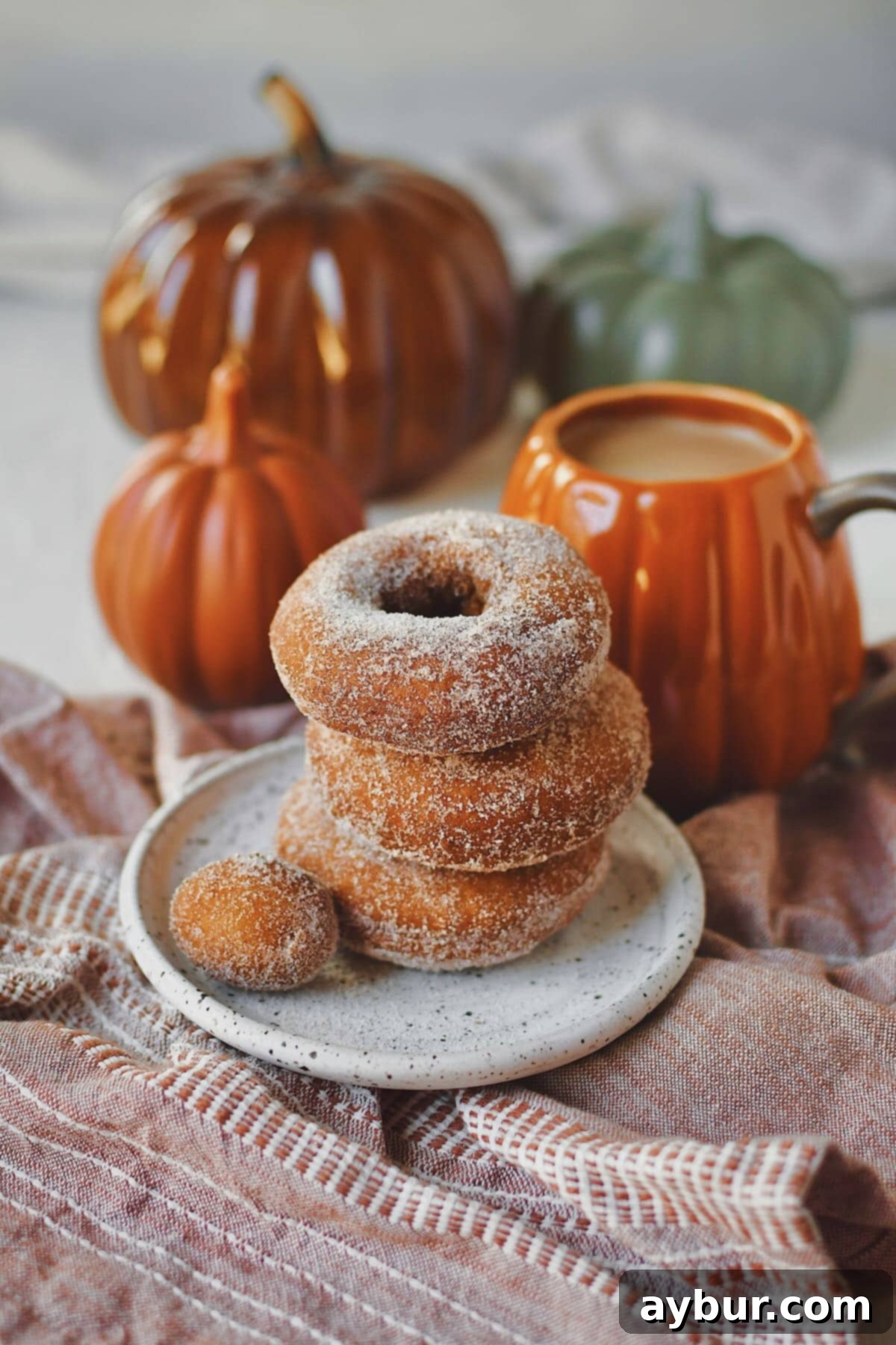 Pumpkin Donuts stacked up with a donut hole on the side, in front of a cup of coffee in a pumpkin mug.