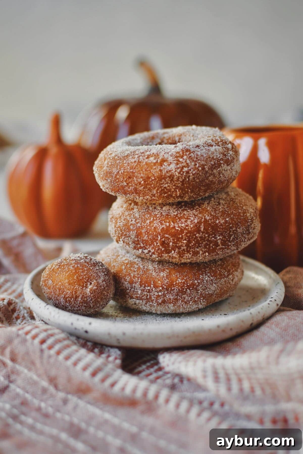 Pumpkin Donuts stacked up with a donut hole on the side, in front of a cup of coffee in a pumpkin mug.