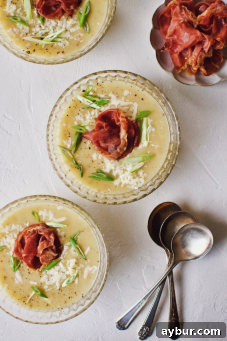 Plant-Based Creamy Potato Soup 2 Creamy Potato Soup after blending, in a crystal bowl, topped with green onions, white cheddar, and a prosciutto rose.