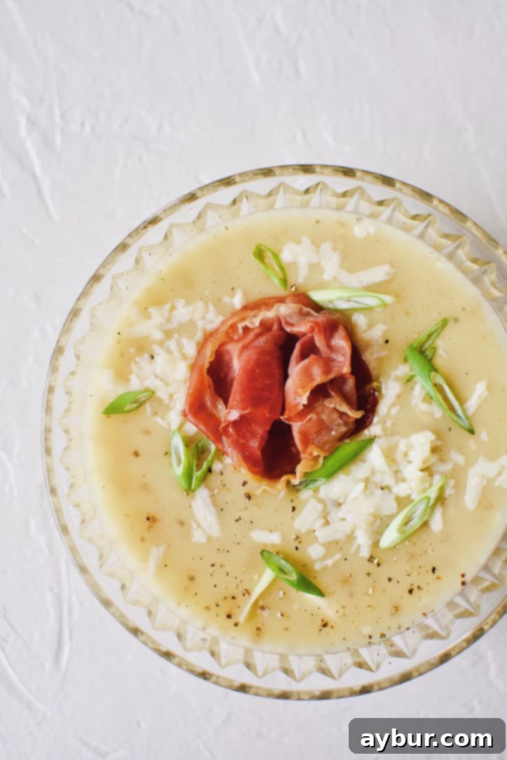 Plant-Based Creamy Potato Soup 8 Creamy Potato Soup after blending, in a crystal bowl, topped with green onions, white cheddar, and a prosciutto rose.