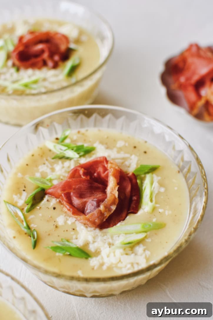 Plant-Based Creamy Potato Soup 9 Creamy Potato Soup after blending, in a crystal bowl, topped with green onions, white cheddar, and a prosciutto rose.