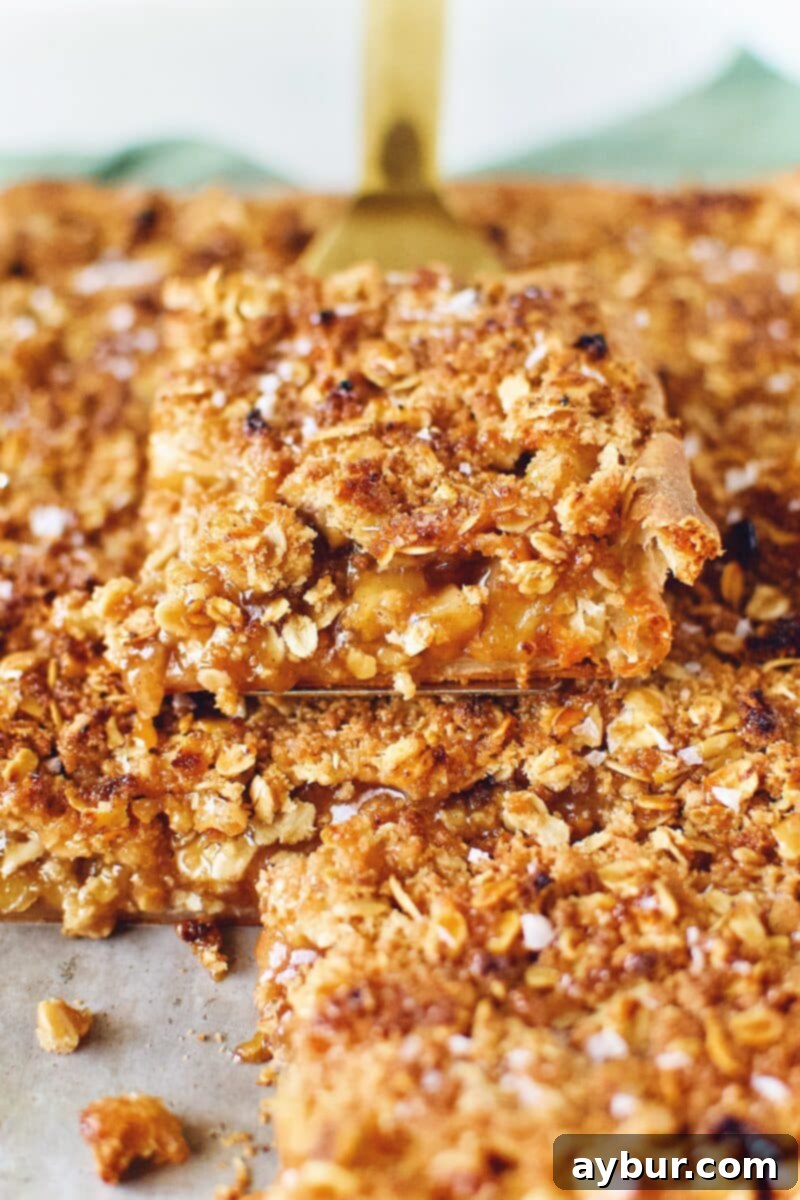 A hand gently removing a large, golden slice of Honeycrisp Apple Slab Pie from the baking pan, showcasing its perfect texture.