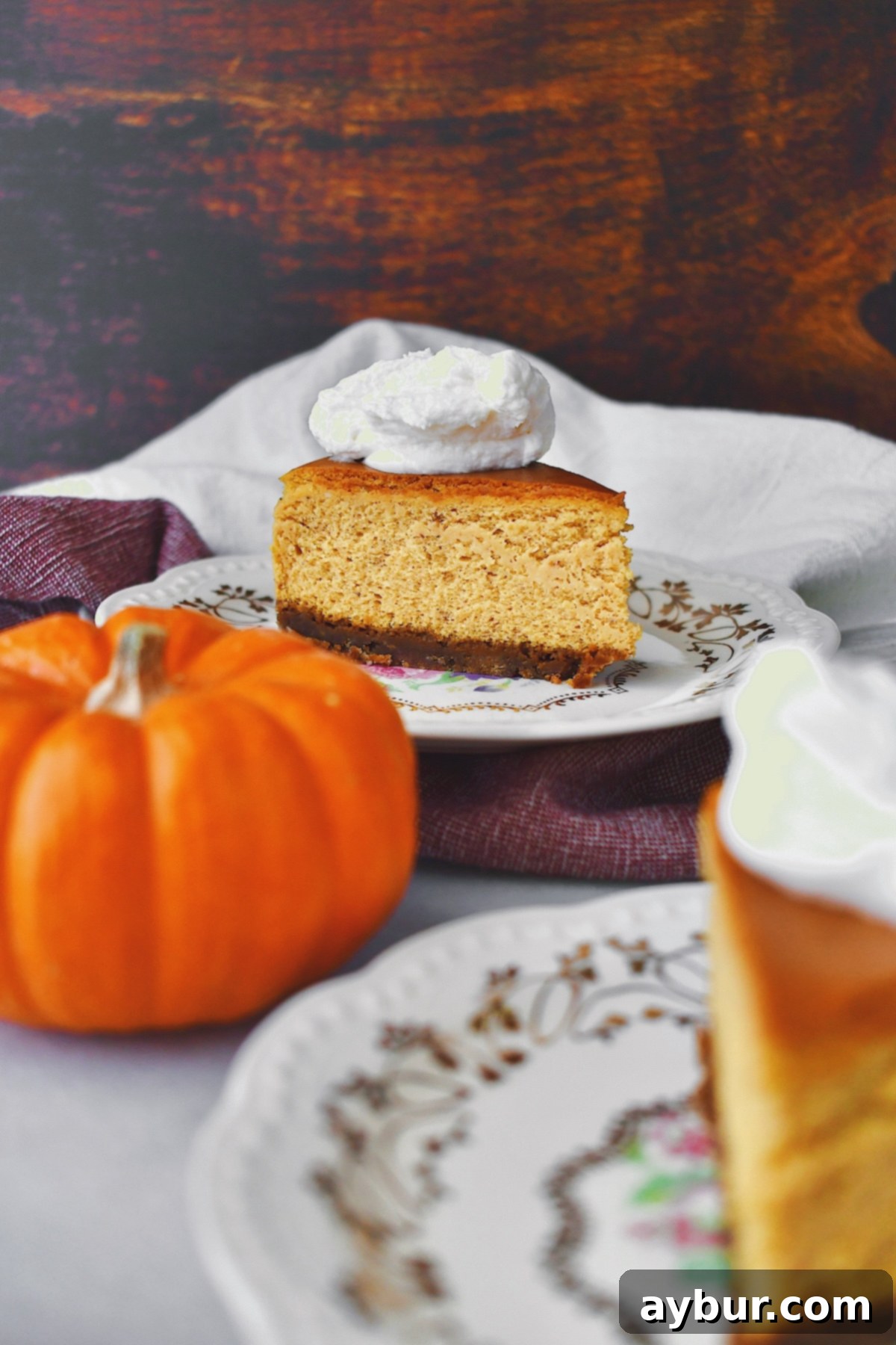 A slice of pumpkin cheesecake elegantly presented on vintage china, crowned with bourbon whipped cream.